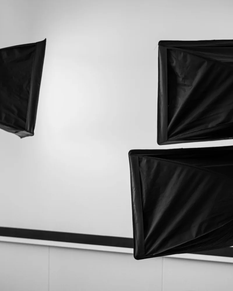 Tres ventanas de luz rectangulares negras montadas en lo alto de una pared blanca de estudio, vistas desde abajo.