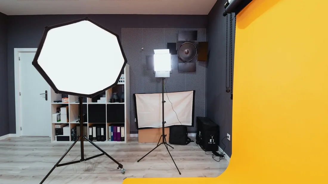 Estudio fotográfico con una ventana de luz octogonal, un panel de luz continua sobre trípode y un fondo de papel continuo amarillo desenrollado hacia el suelo.